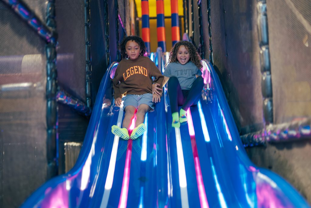 Two kids sliding down the wave slide that has lights